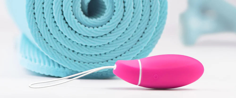 Rosa knipkula placerad framför en hoprullad blå yogamatta – symbol för bäckenbottenträning och intim hälsa